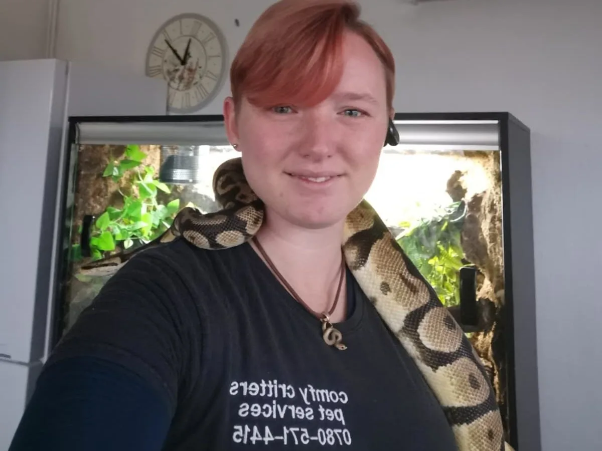 Leia, owner of Comfy Critters, wearing a Comfy Critters t-shirt with a pet snake resting around her shoulders